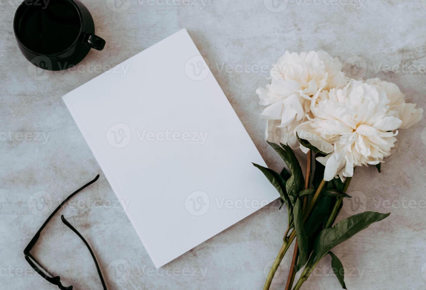 Bouquet of white peony flowers, magazine, cup of tea and black eyeglasses on grey table photo