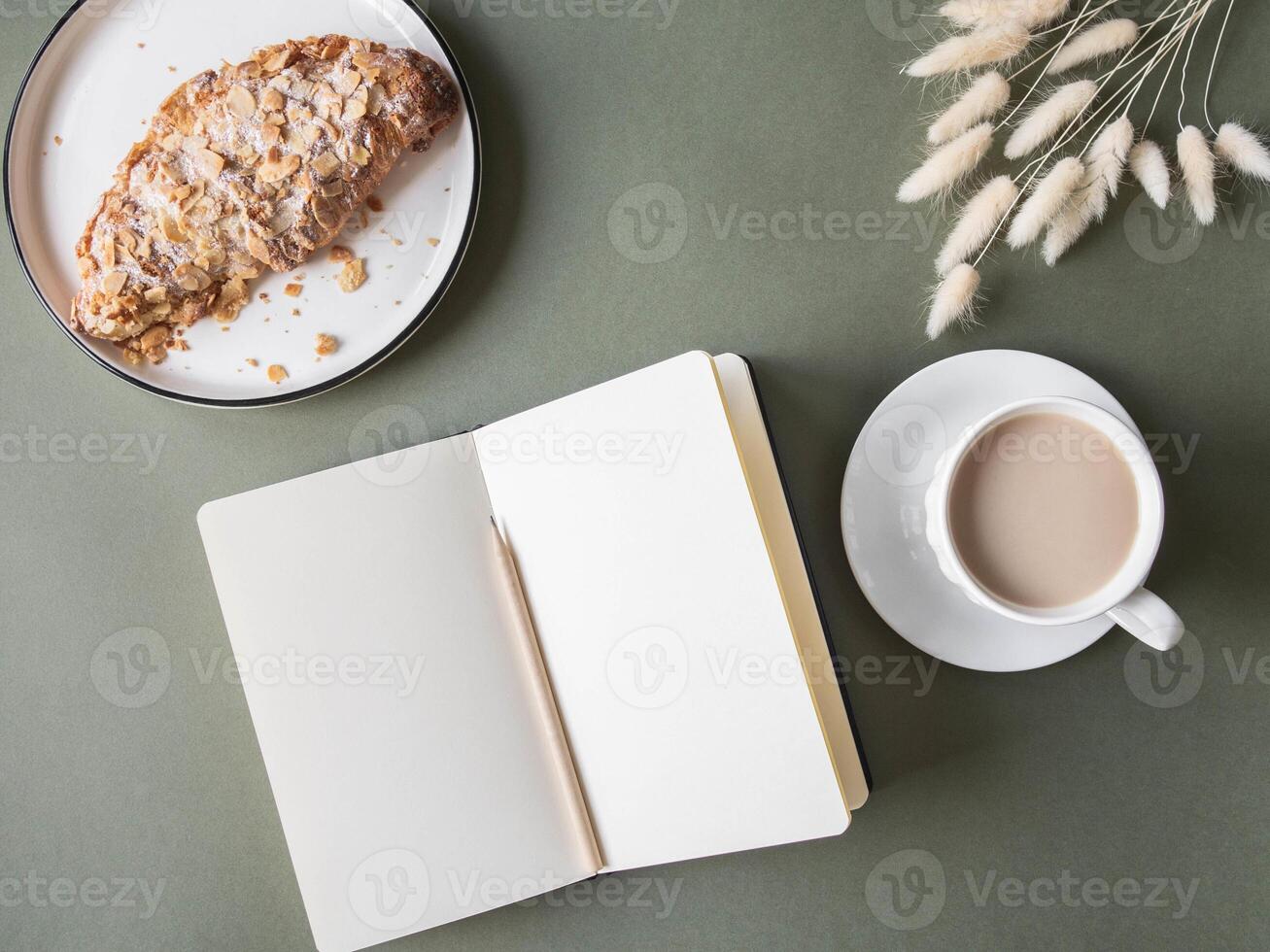 Notebook with blank sheets, cup with coffee, croissant on green background photo
