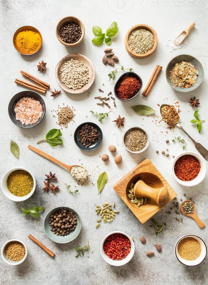 Various dry spices in small bowls and raw herbs flat lay on grey background. photo