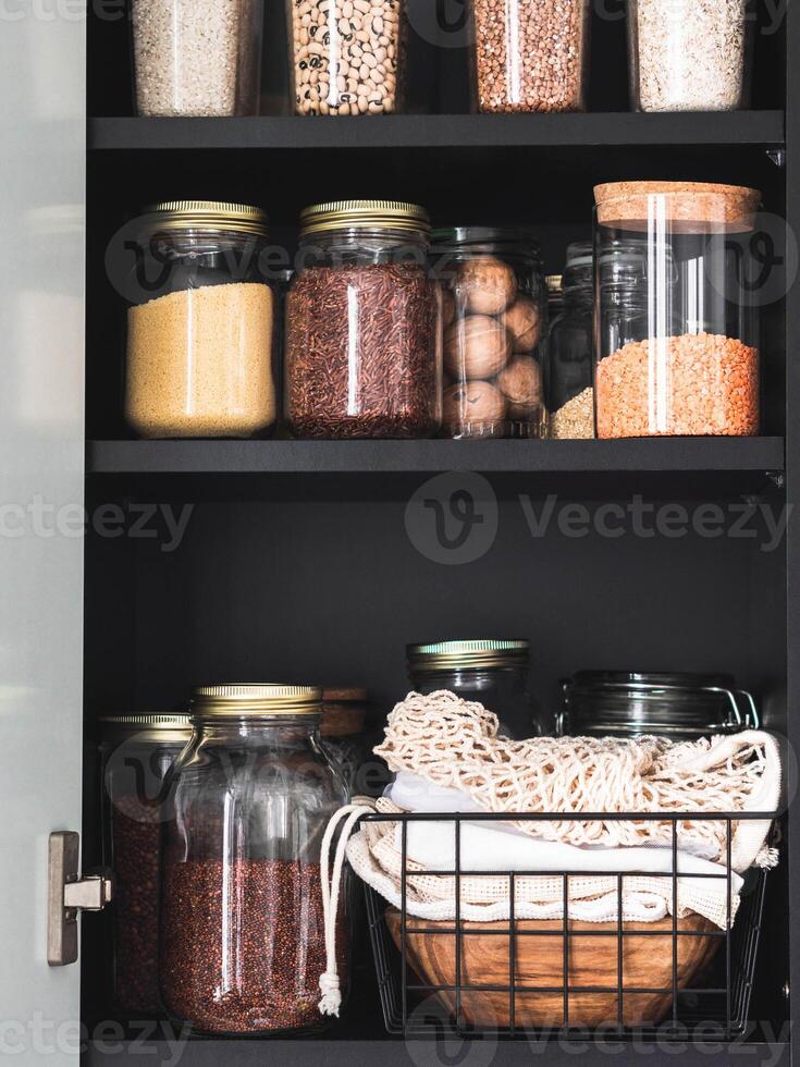 Black shelf in the kitchen with various cereals and seeds in glass jars. photo