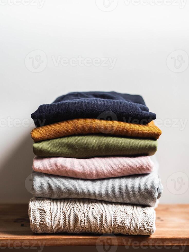 Pile of varicolored autumn clothes on wooden background, sweaters, knitwear, copy space photo