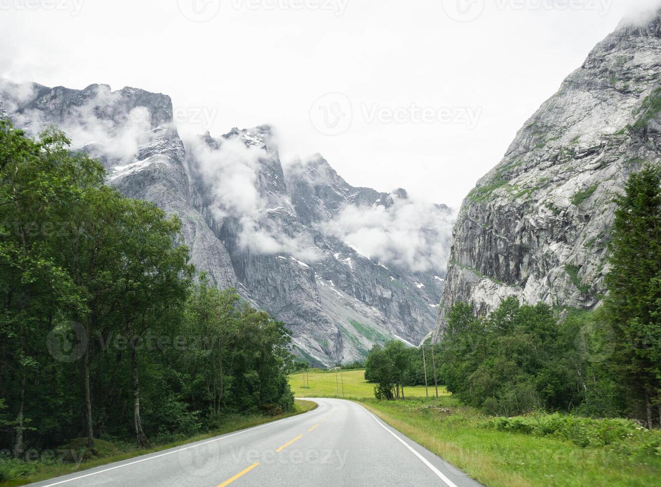 View of an empty paved road with white lines. Mountain road through a valley with trees and green lawns photo