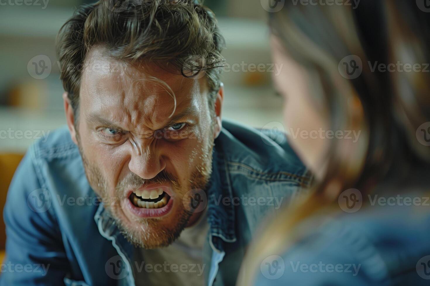 Man with a beard and blue denim shirt yelling at a woman, facial expression is extremely angry, with his mouth open in a scream and his eyes wide. Heated argument between a couple photo