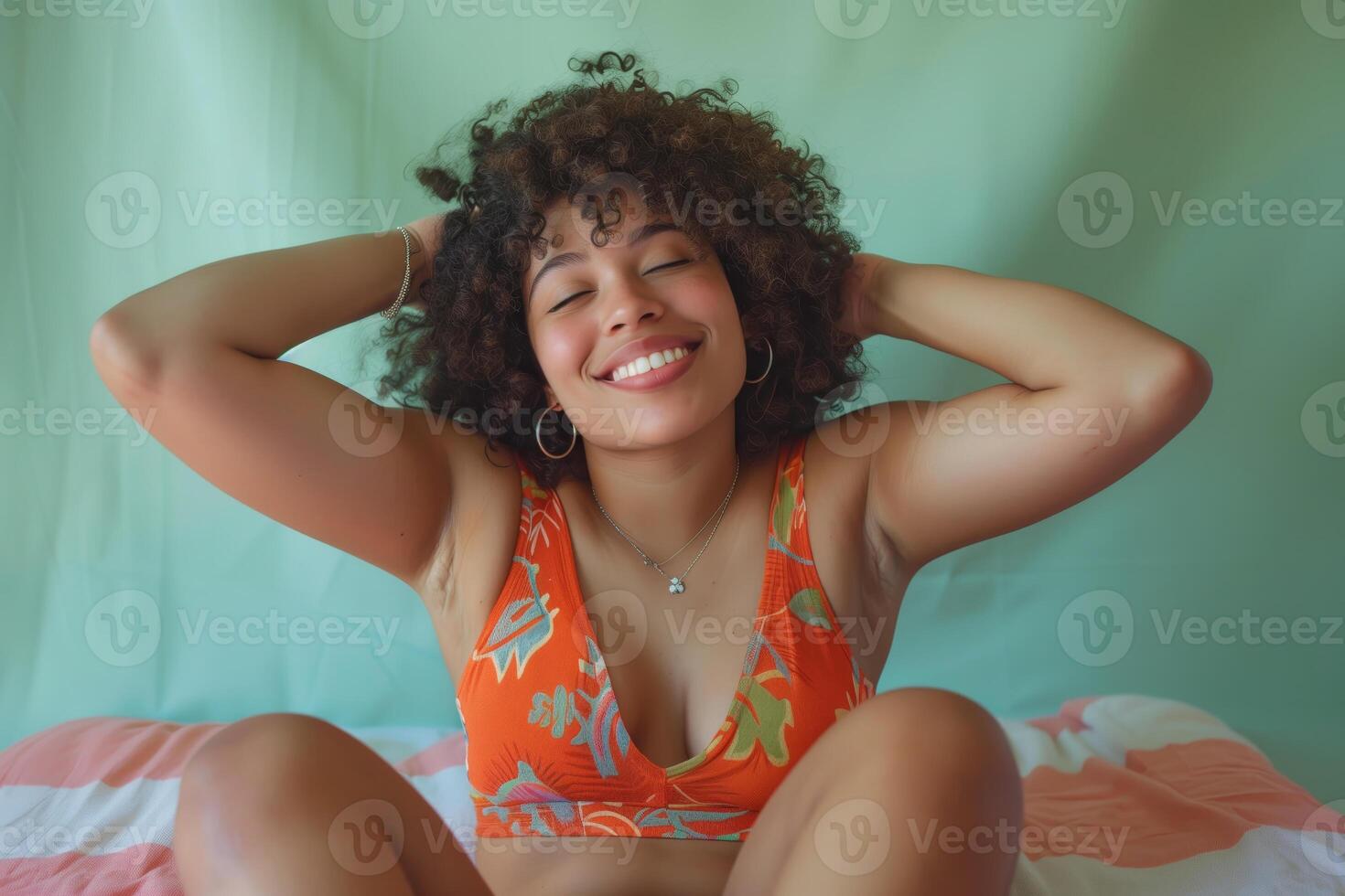 Smiling African American woman with curly hair in orange top sitting on a bed photo