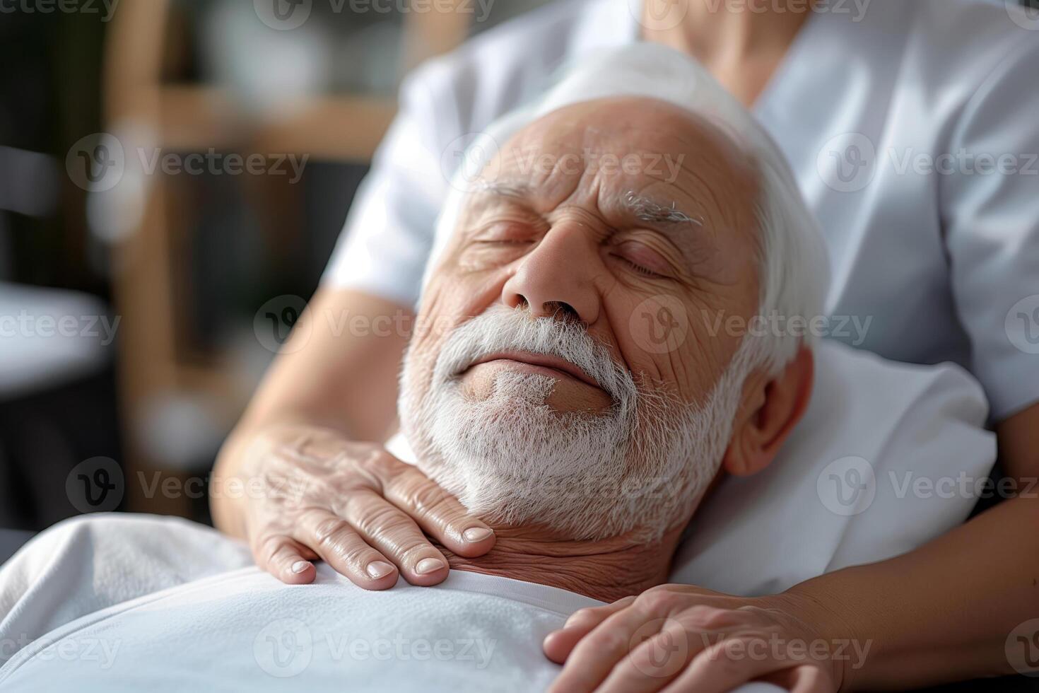 A senior man with a white beard is receiving a face massage at a spa. He has his eyes closed and is visibly relaxed. The masseuse is gently applying pressure to his face and neck photo