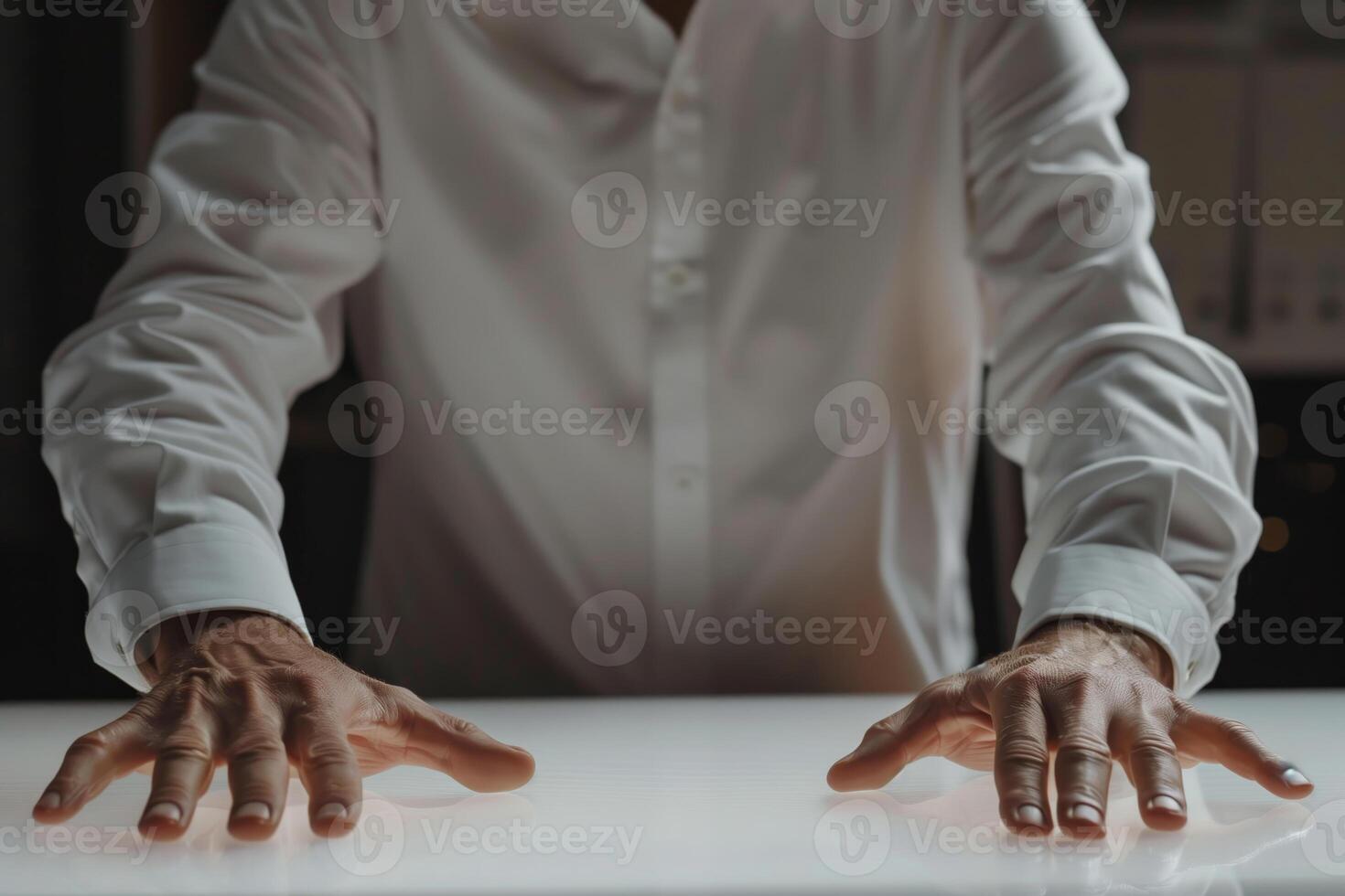 A person wearing a white shirt reaches out with both hands, flat on a table, as if trying to grasp something photo