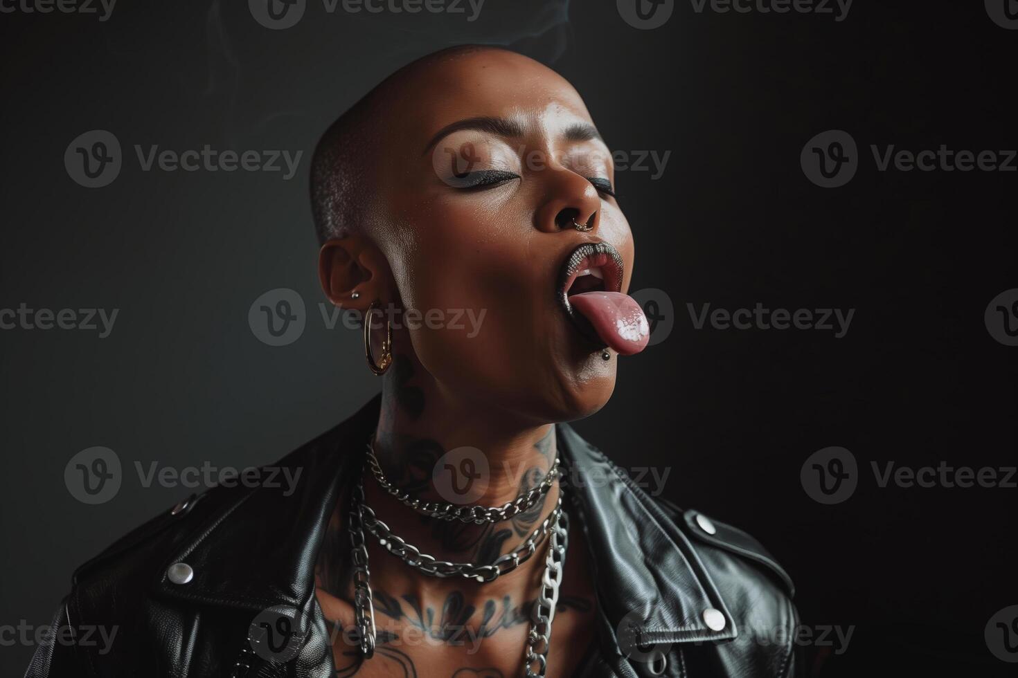 Close up portrait of a woman with a shaved head and multiple piercings sticking her tongue out photo