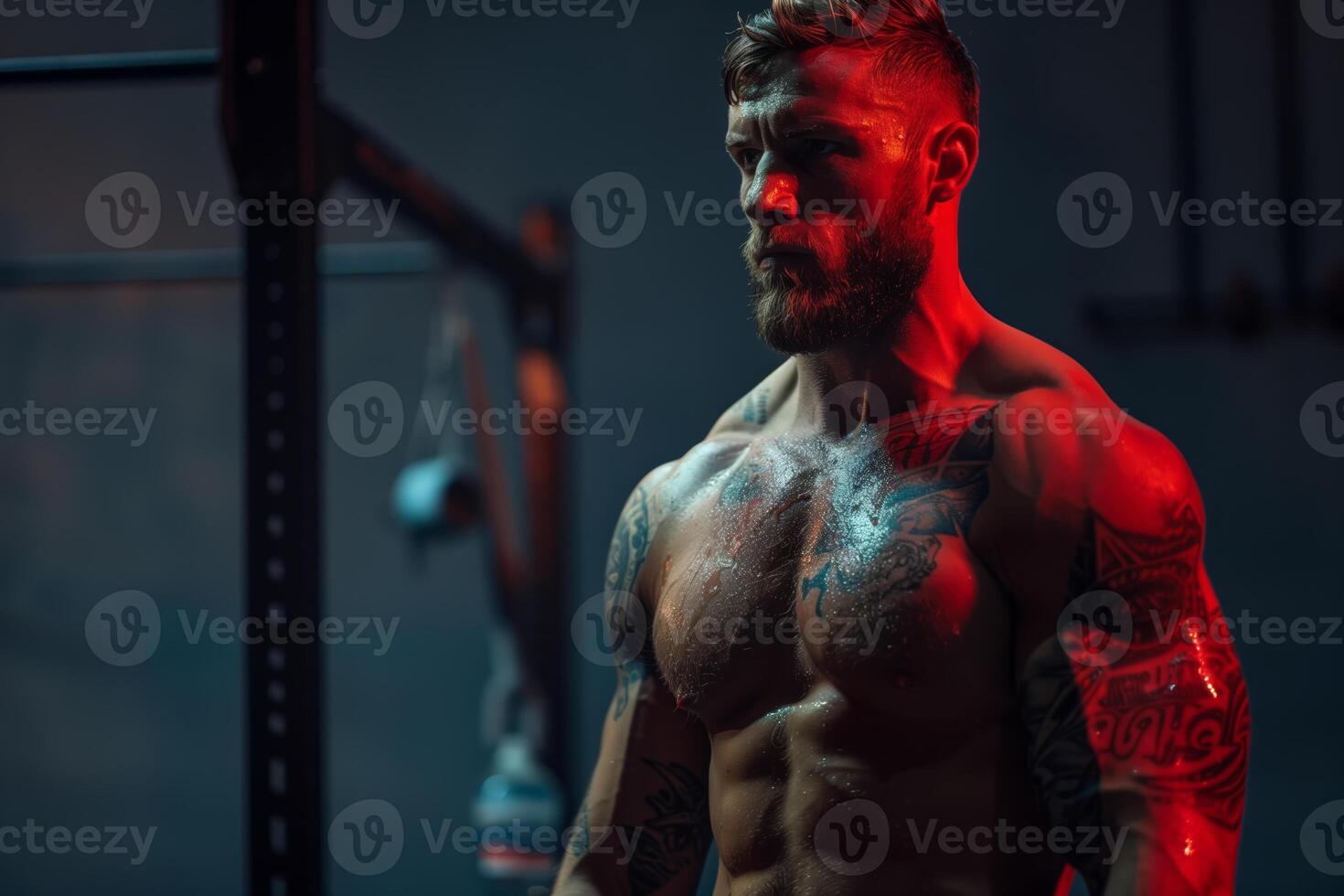 A muscular bodybuilder poses in a dimly lit gym with red lighting, showcasing his defined physique and intricate tattoos photo