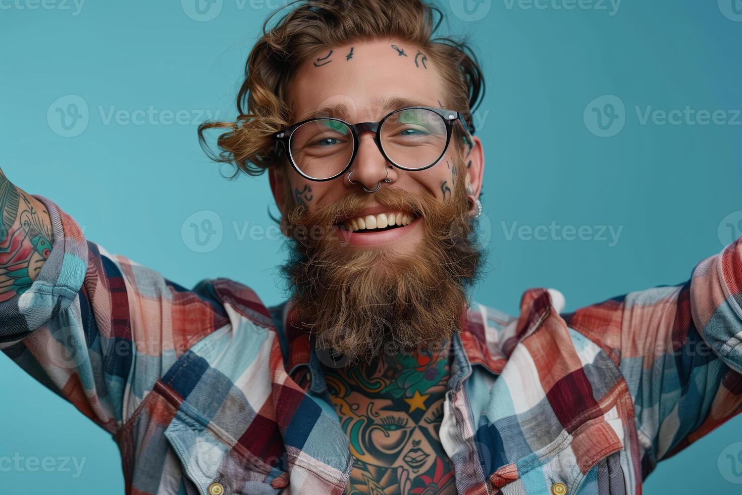 Smiling bearded man with tattoos wearing glasses and plaid shirt against blue background photo