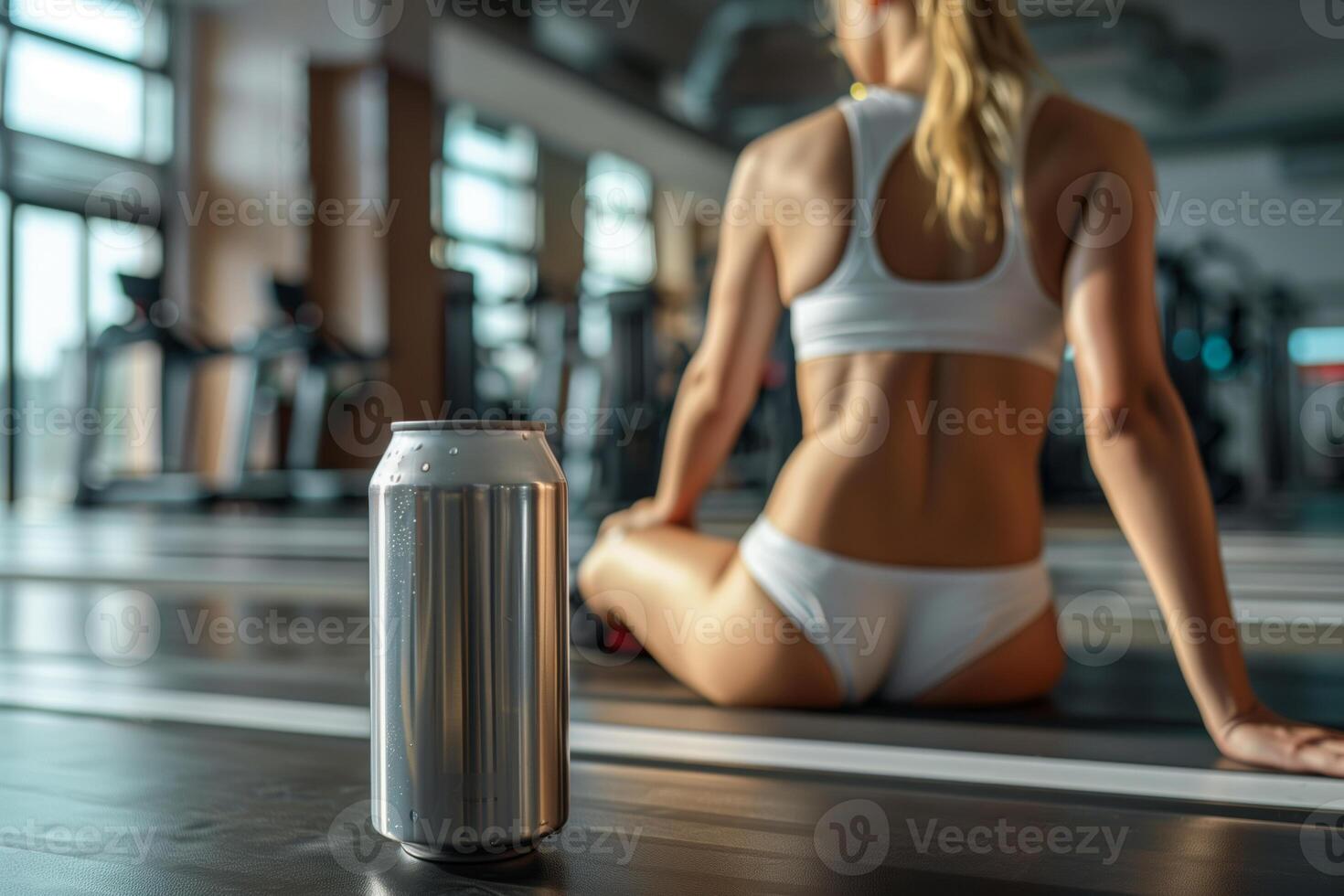 Aluminum can resting on treadmill in gym with woman sitting in background photo