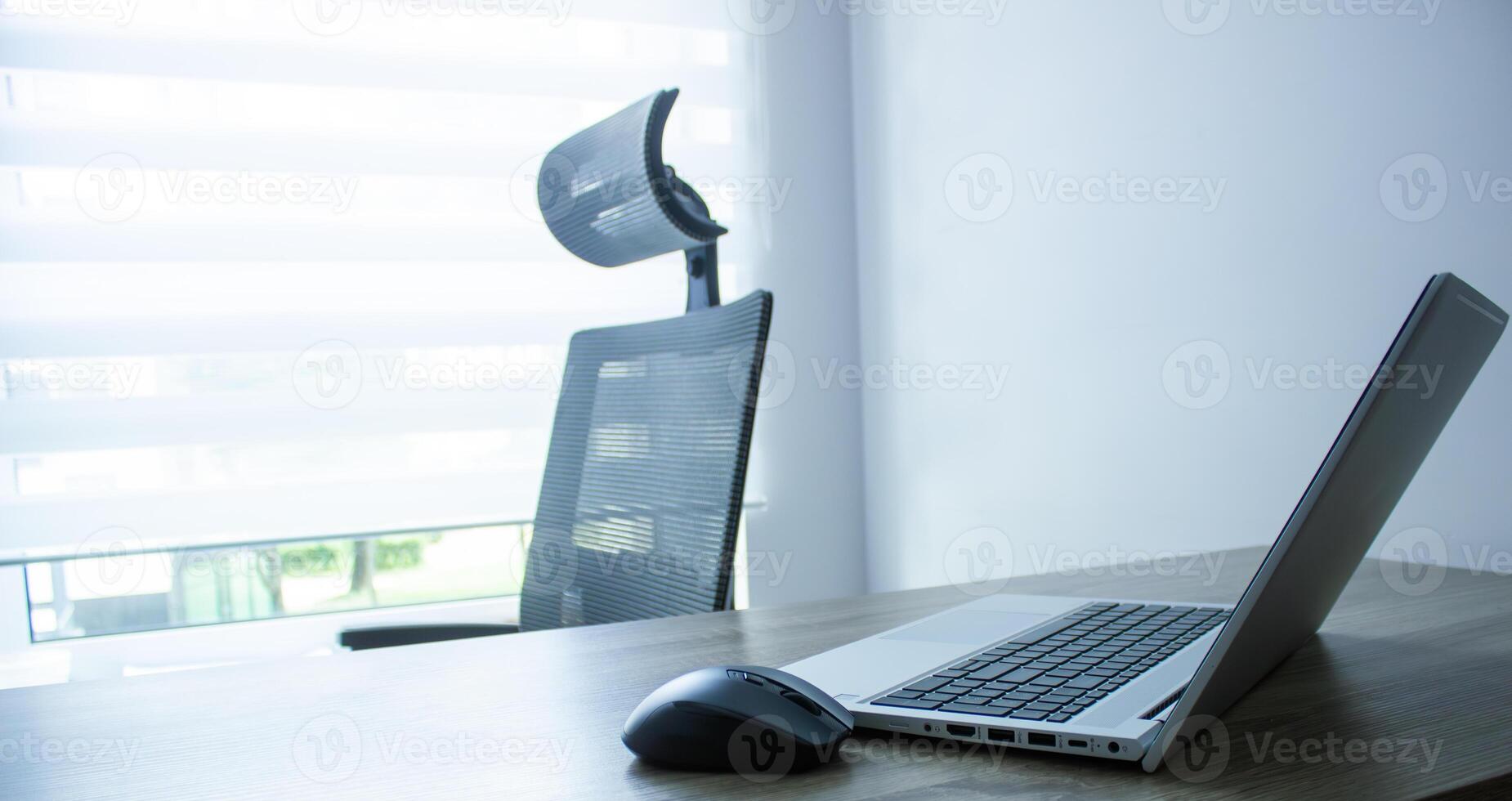 computer mouse close up nearby silver laptop and keyboard, chair and window background, office concept photo