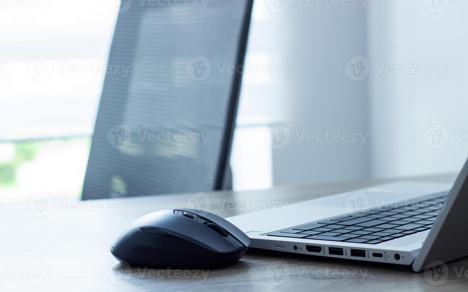 computer mouse close up nearby silver laptop and keyboard, chair and window background, office concept photo