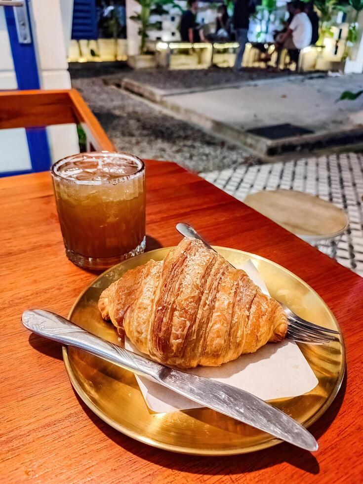 a plate of croissant bread and a glass of tea or beer or whiskey served on a wooden table in a luxury cafe or restaurant photo