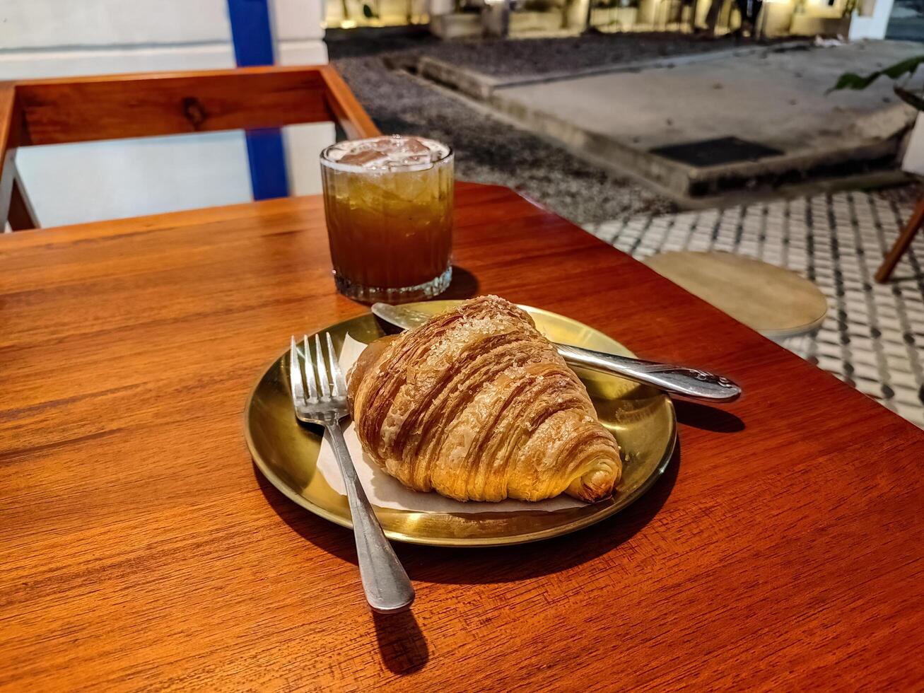 a plate of croissant bread and a glass of tea or beer or whiskey served on a wooden table in a luxury cafe or restaurant photo