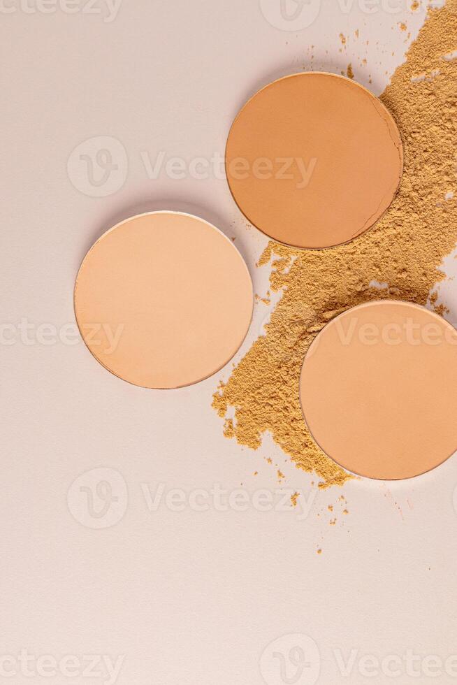 Three chic round blocks of compact powder closeup on a loose powder sample. top vertical view. Beige background. The texture of the powder product. photo