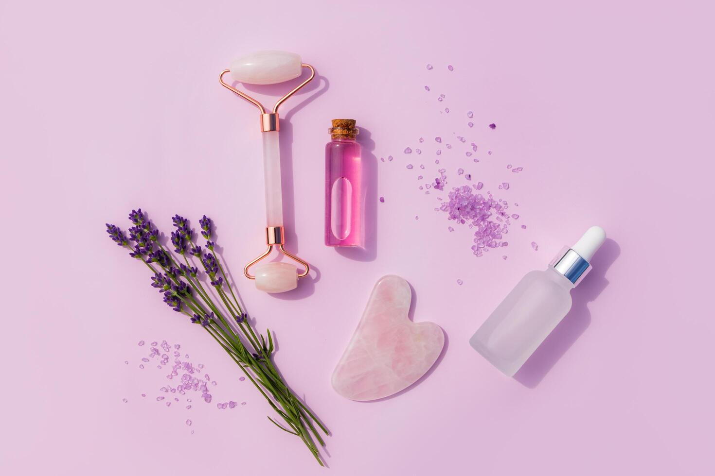 A set of cosmetic products in glass bottles, a roller massager and a rose quartz scraper, sprigs of fresh lavender. flat lay. top view. Home Spa Care photo