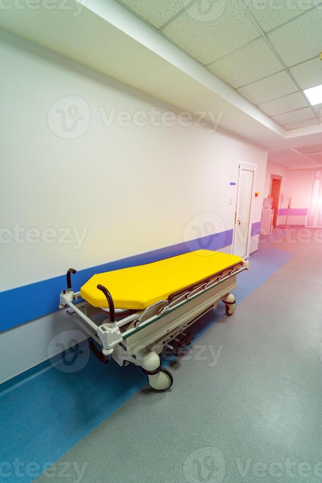 Trolley for patients in hospital corridor. Bright light from the lamps. Blue stripes on walls. New modern hospital. Closeup. photo