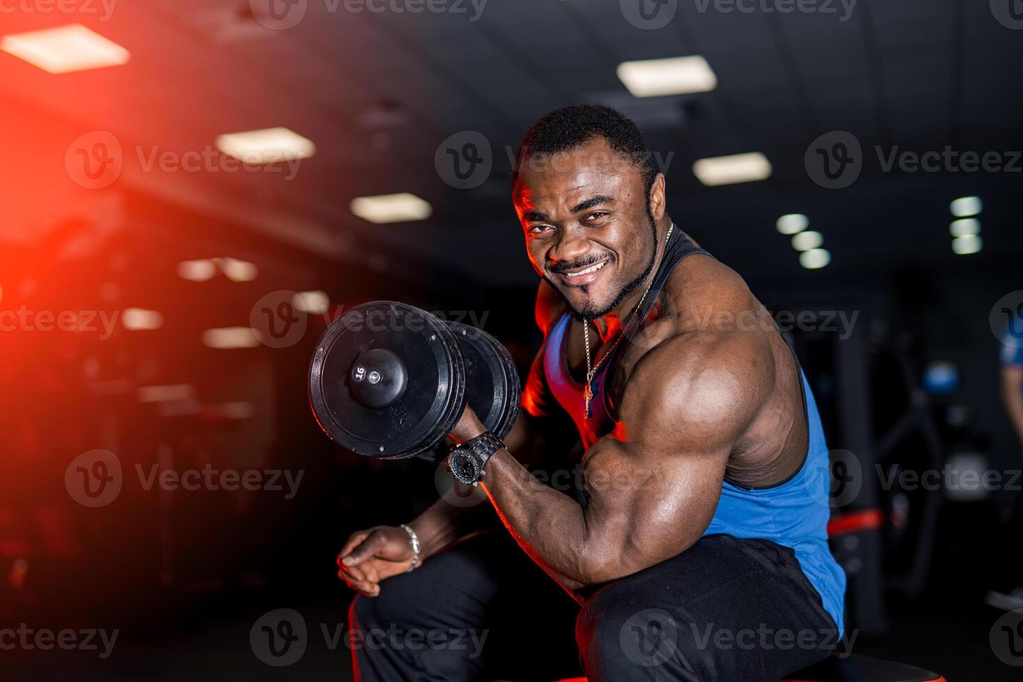 Smiling afro american sports man looking at camera over black background with dumbbell in hand. Perfect muscular body with strong muscles. photo