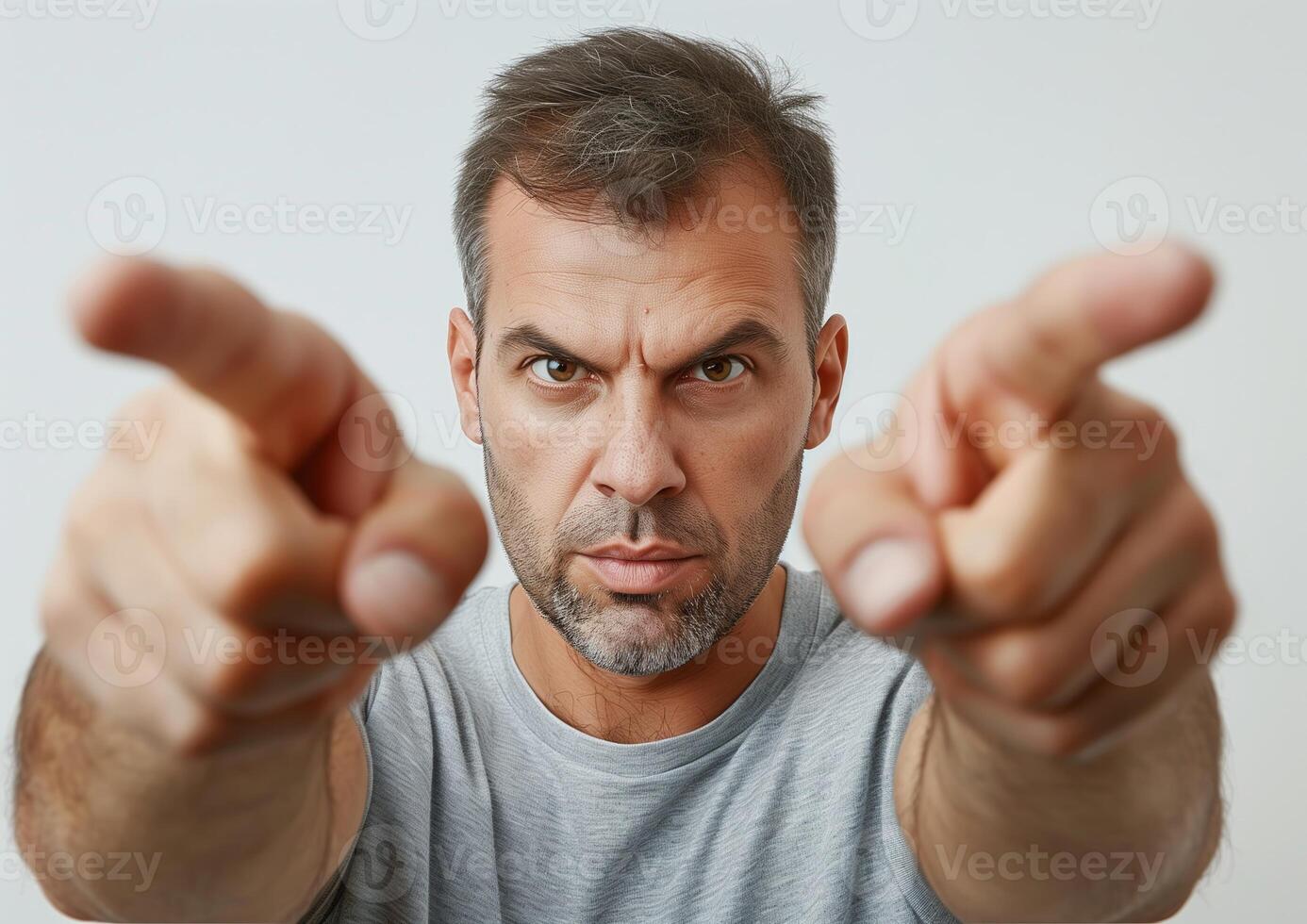 Serious Man Pointing Fingers Forward, Intense Expression, Close-Up Portrait, Isolated Background, Horizontal View, Strong Eye Contact, Determined Pose, Mid-30s Male, Casual Grey T-Shirt photo