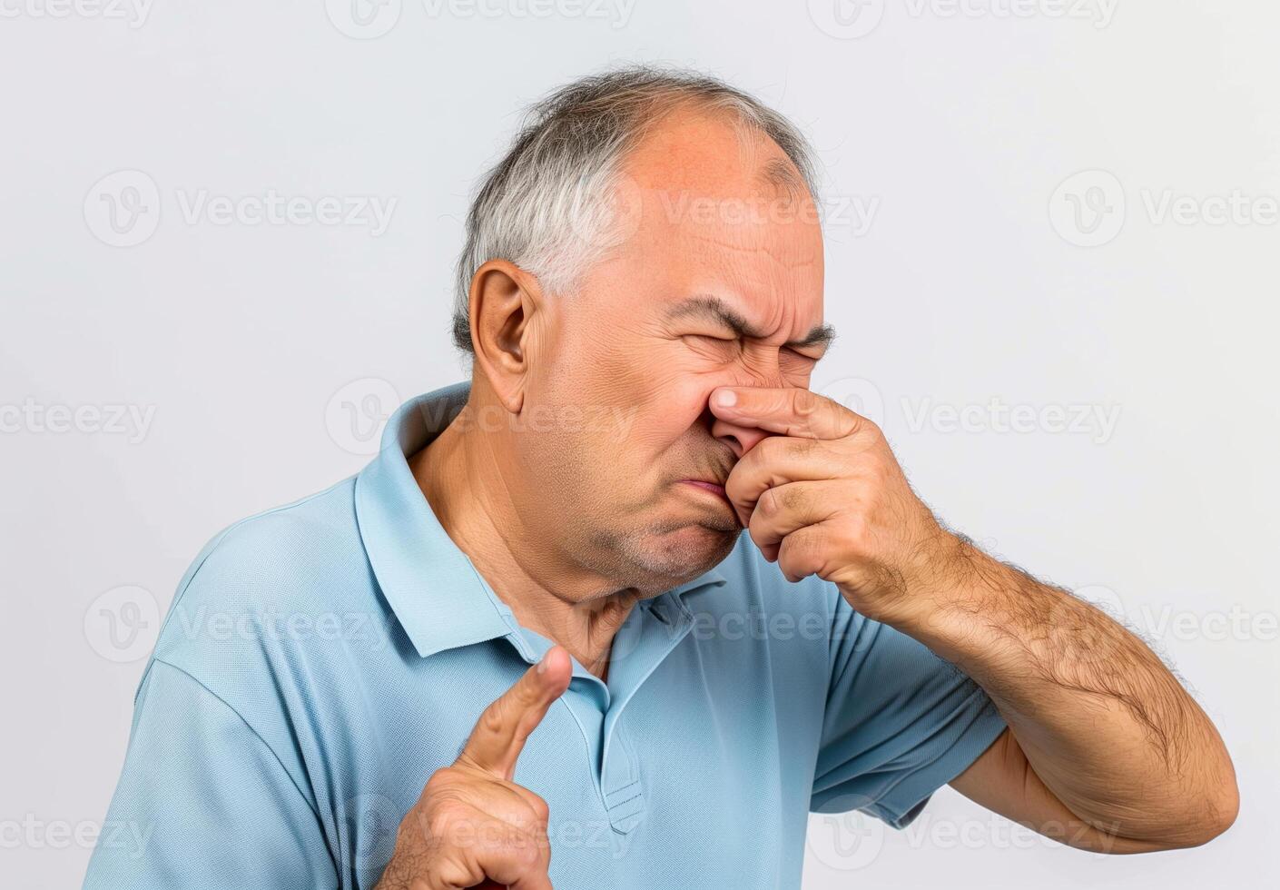 Senior Man In Blue Polo Shirt Plugging Nose Due to Unpleasant Smell Concept Demonstrating Disgustful Reaction On White Background Expressing Stink Environmental Pollution Ageing Health Care Smelly photo