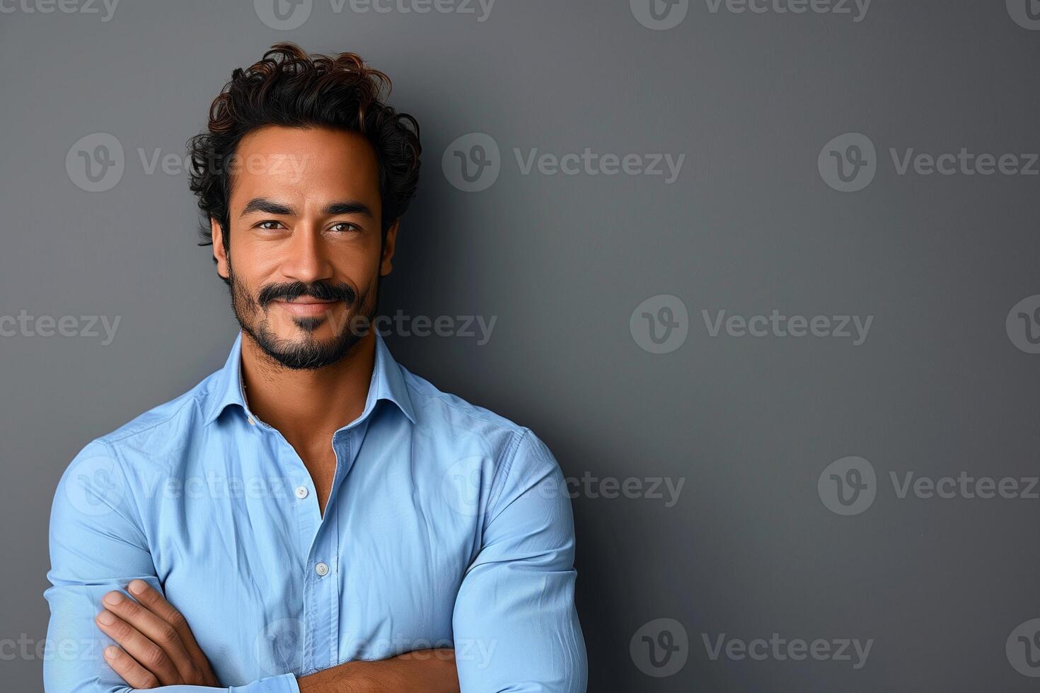Confident Hispanic Man Standing Against Gray Background in Light Blue Shirt Smiling with Arms Crossed, Modern Casual Style for Profile or Business Use photo