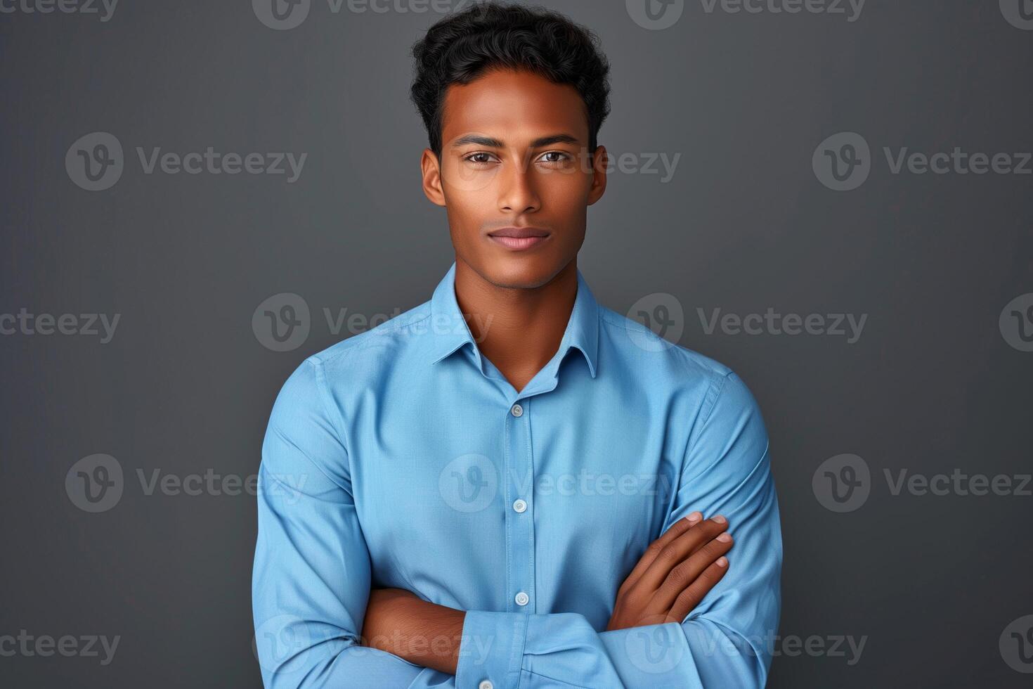 Confident Young Man in Blue Shirt Posing Against a Dark Background with Arms Crossed, Expressing Determination and Elegance in Studio Photography photo
