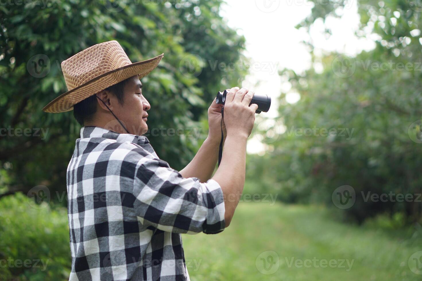 Asian man botanist holds binuculars to explore nature in forest. Concept, nature exploration. Survey ,research botanical plants. Forest and environment conservation. photo