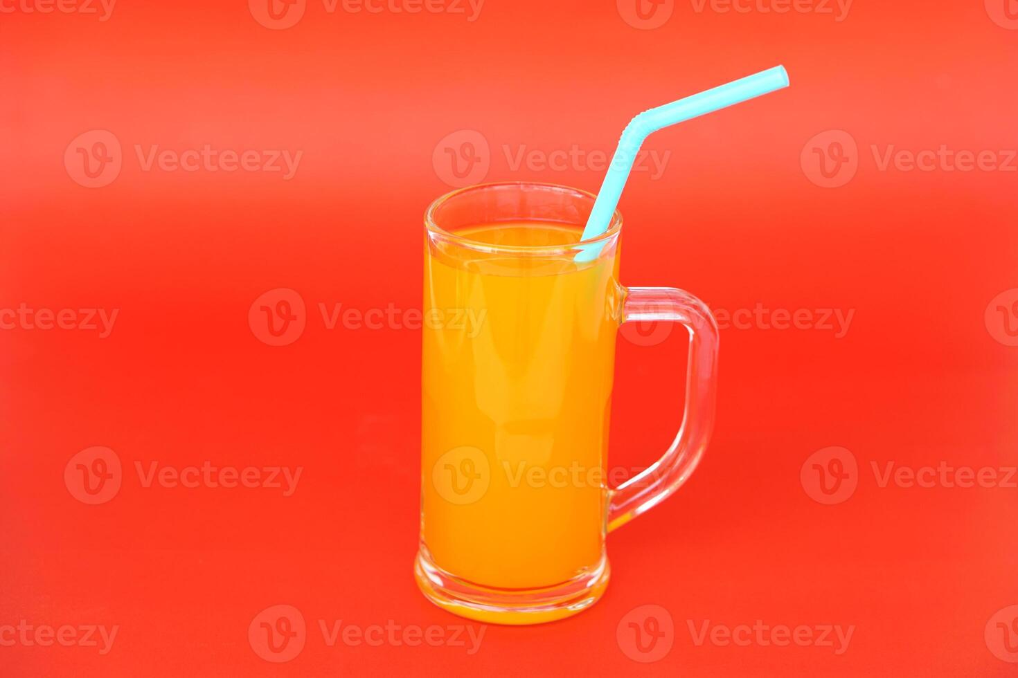 Glass mug of orange juice with drinking straw. Red background. Concept, morning refreshing beverage. Sweet, testy and high vitamin C. photo