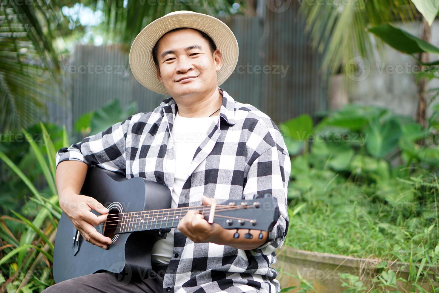 Handsome Asian man listen to music and playing the guitar in garden with cozy atmosphere. Concept, Relax time with music. Happy lifestyle. Love music. Hobby and pastime photo