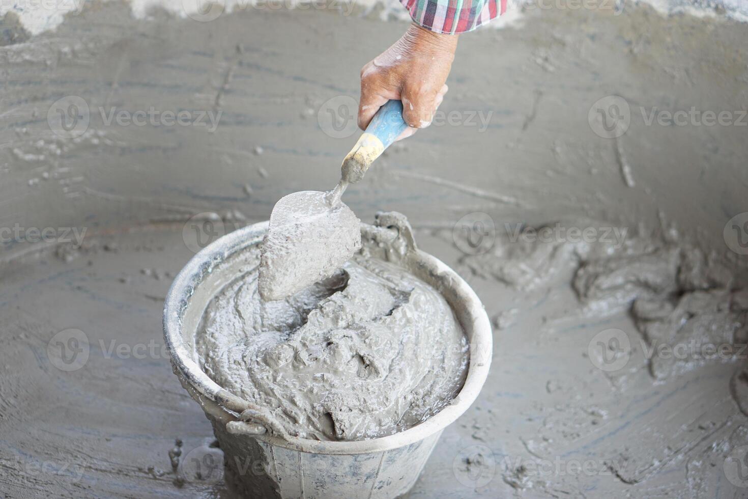 Close up worker hand hold a trowel to mix wet cement in bucket. Concept. Construction job. Process of construction work with cement. Choose good quality and proper material product for building photo