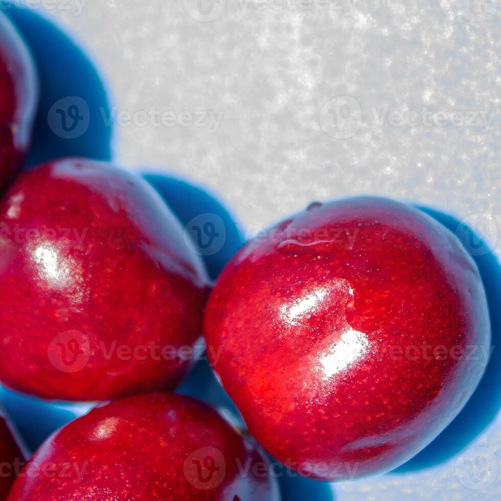 A bunch of red cherries are arranged in a circle on a blue background. The cherries are shiny and ripe, and they seem to be the main focus of the image photo