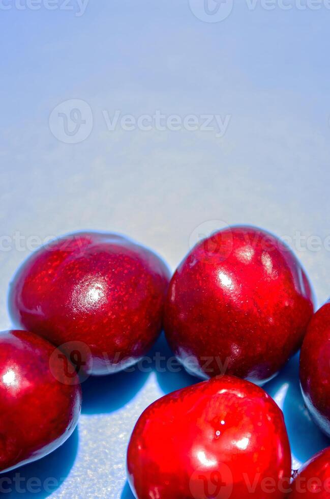A bunch of red cherries are arranged in a circle on a blue background. The cherries are shiny and ripe, and they seem to be the main focus of the image photo
