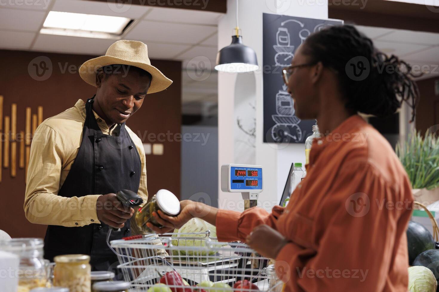 A man selling goods uses a reusable scanner to scan items, encouraging zero-waste purchasing. A close-up shot shows two African Americans holding a glass jar and a scanner at the checkout desk. photo