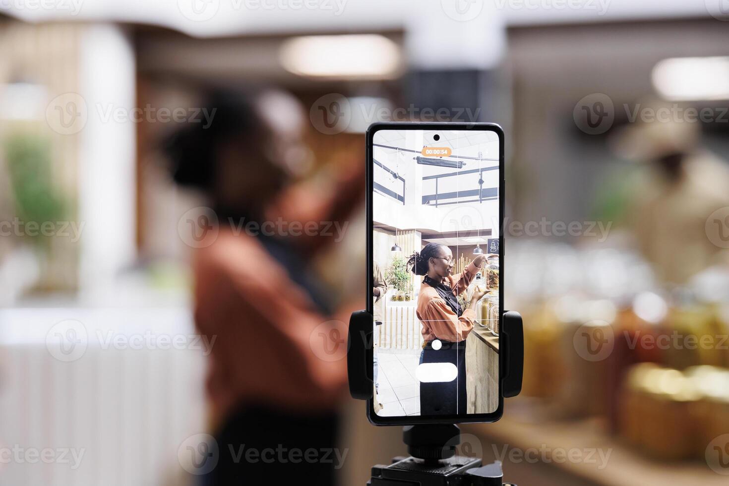 The eco-conscious owner promotes zero waste with reusable packaging. Social media vlogger films using a smartphone and tripod. Vibrant shelves and a camera capture the moment. Focus on the foreground. photo