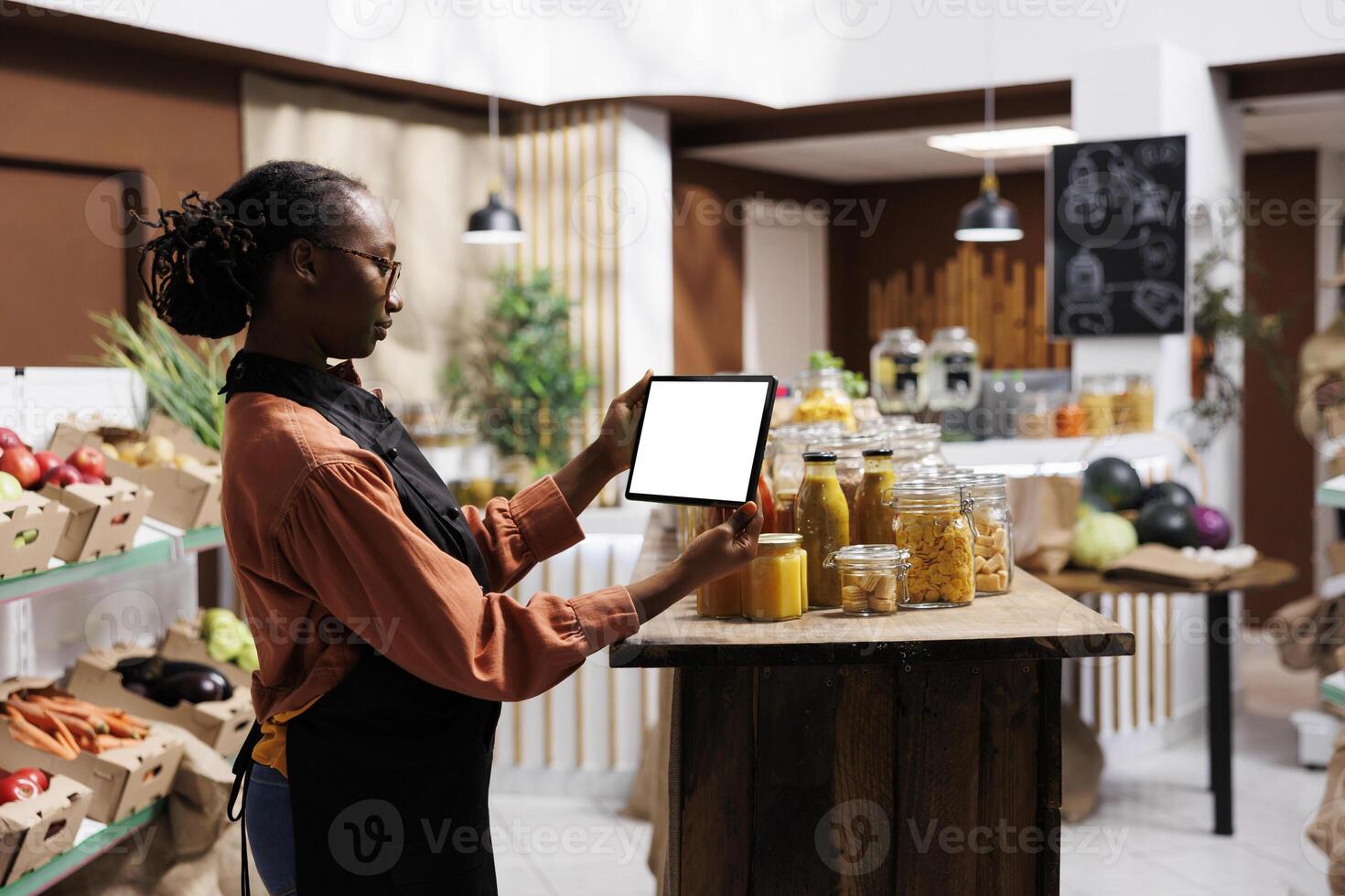 African American woman holding a tablet displaying a blank chromakey template for the advertisement of eco friendly food store. Perfect digital mockup for customer service and packaging tools. photo