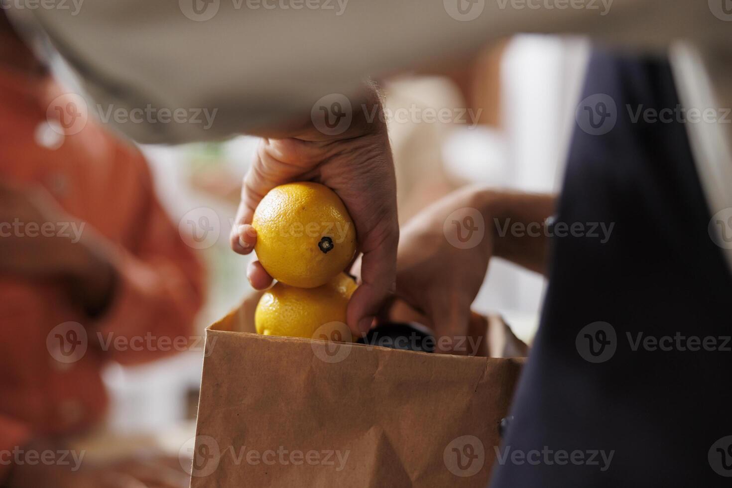 Selective focus on storekeeper putting organic fruits and vegetables in takeaway parcel. Close-up of male vendor packing freshly picked produce for customer in a paper bag at the checkout counter. photo
