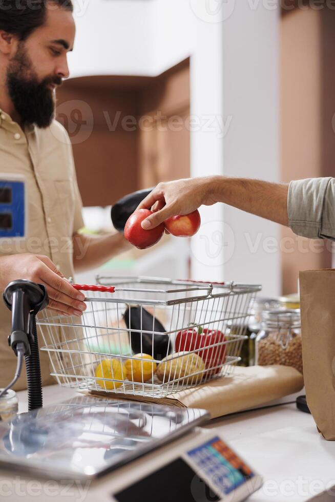 Image shows shopkeeper helping out caucasian customer with his groceries at the cashier desk. Male shopper at checkout counter ready to weigh his freshly harvested produce. photo