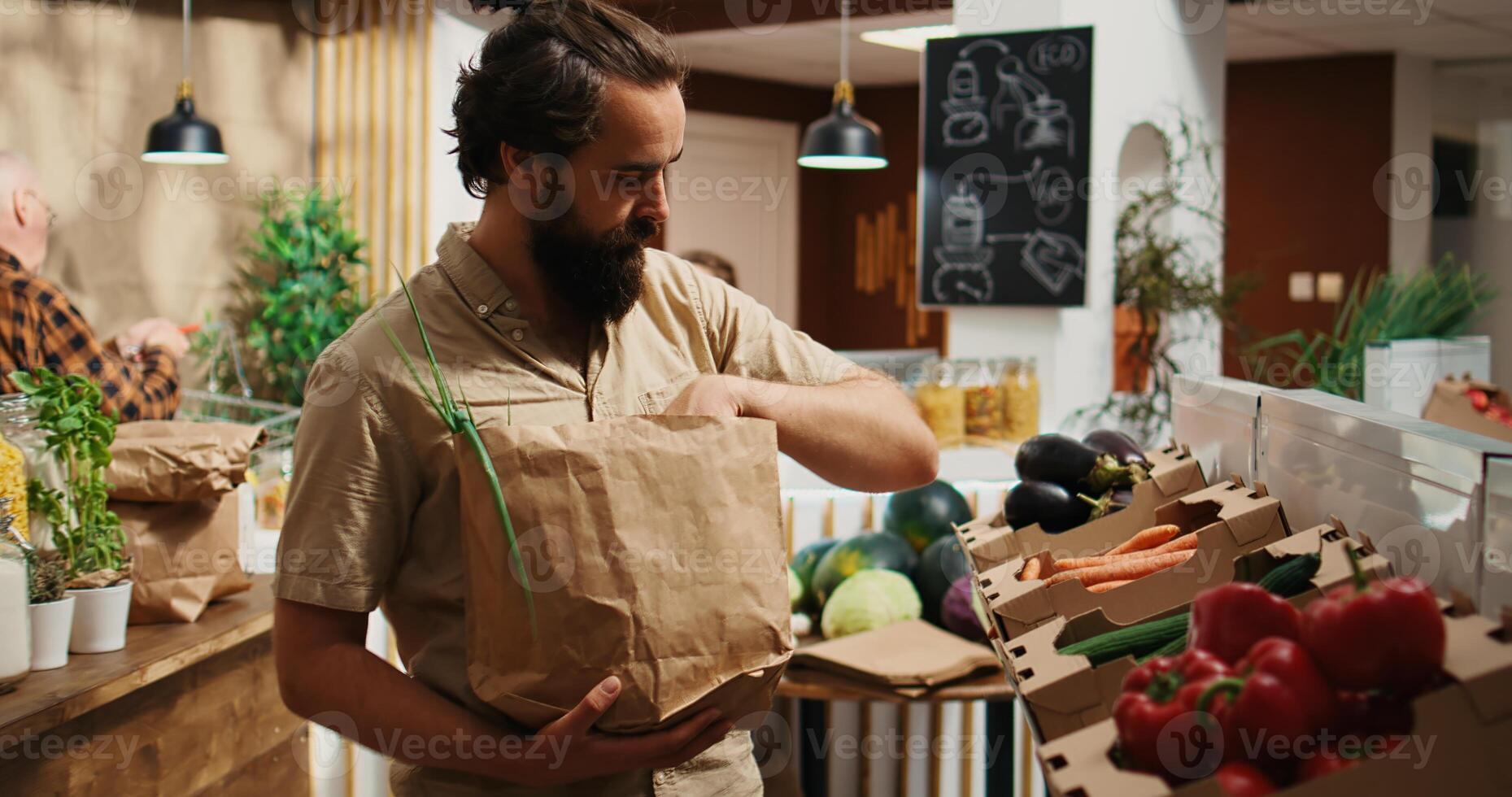Dolly in close up shot of man in zero waste supermarket using nonpolluting paper bag while shopping for vegetables. Client in local shop using no single use plastics policy for CO2 emissions reduction photo