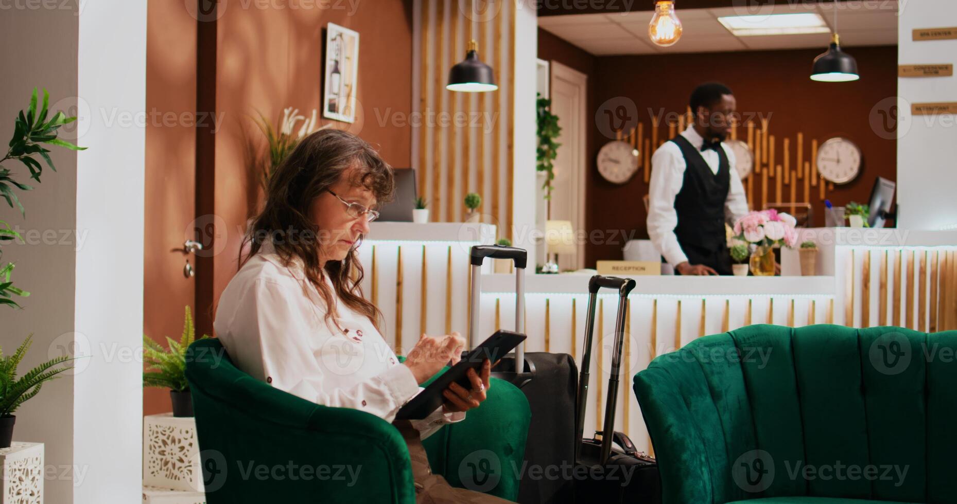 Hotel guest relaxing in lounge area, using modern tablet to find restaurants and places to visit. Elderly person travelling to all inclusive resort and waiting to see room and start exploring. photo