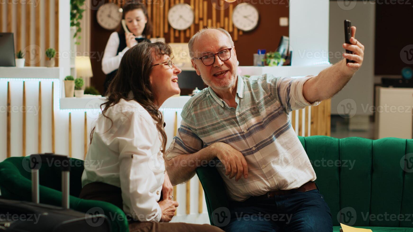 Old couple talk on videocall with kids while travelling abroad, online videoconference to discuss about holiday plans. People passing time waiting in lounge area. Handheld shot. photo