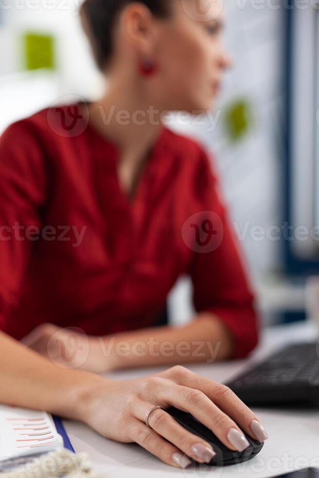 Closeup of manager fingers with ring cliking at desk in startup office. Employee scrolling content on desktop computer. Entrepreneur hand in red shirt using wireless computer mouse. photo
