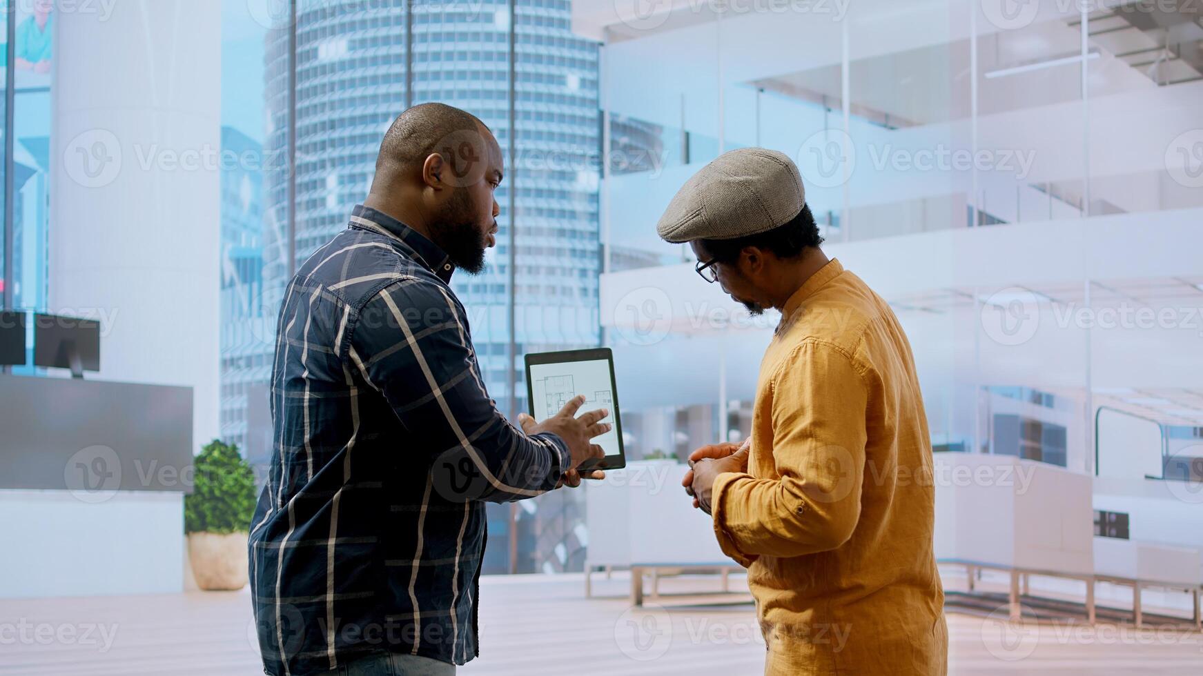 Real estate broker and client negotiating a leasing contract for a high class modern office space, evaluating blueprints on tablet during office tour. Property investment opportunity. Camera A. photo