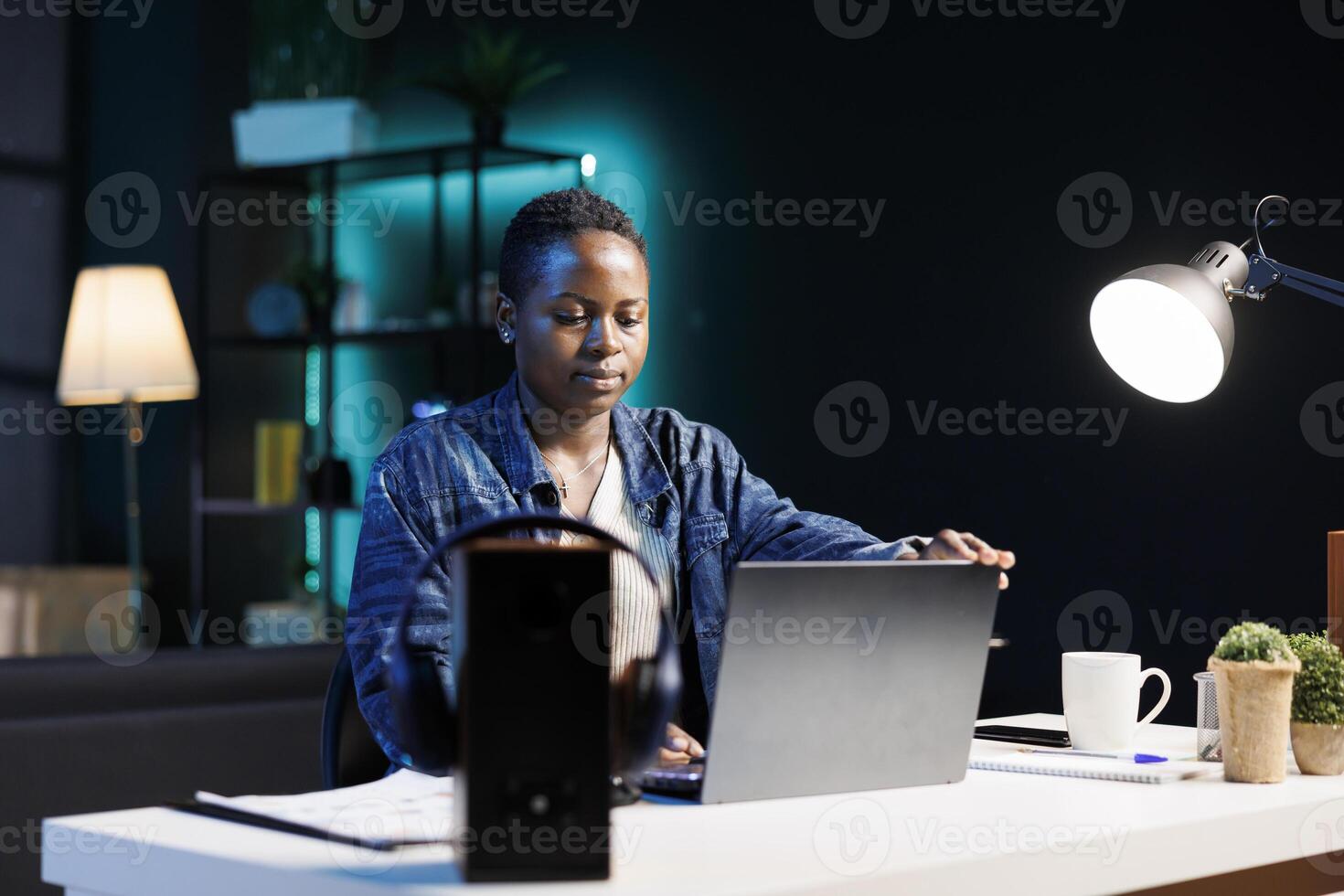 African American woman sitting at desk and holding a personal computer placed on a white table. Young female blogger opening laptop, preparing to work from home, browsing internet for ideas. photo