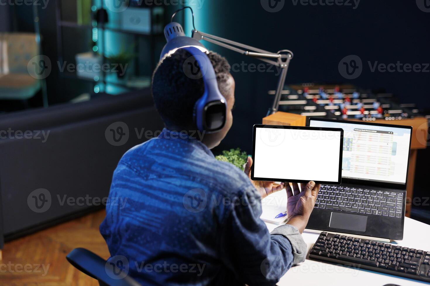 Black woman with headphones horizontally holding tablet with white screen. Female freelancer working from home, focused on digital device displaying blank chromakey mockup template. photo