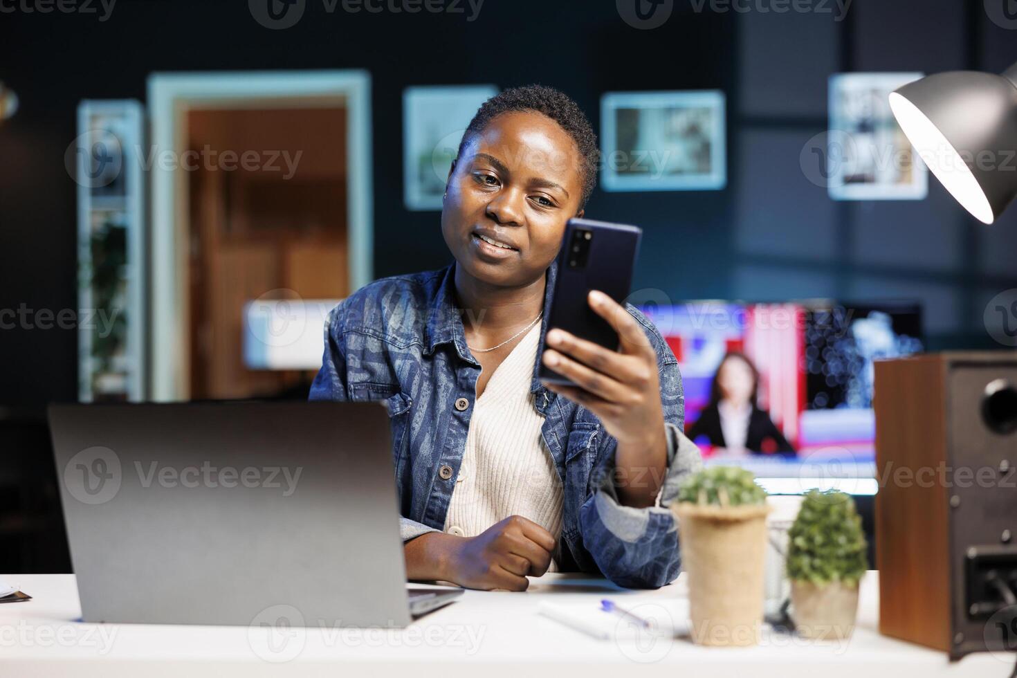 Multitasking African American female freelancer working remotely from home using a laptop and smartphone for online communication. Black woman holding and surfing the net on mobile device. photo