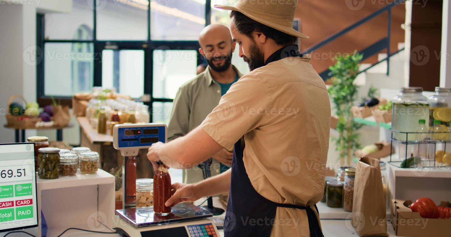 Man checking weight of produce using modern market scale and selling fresh items to customer. Local grocery store vendor weighting potatoes and pasta in reusable container. Handheld shot. photo