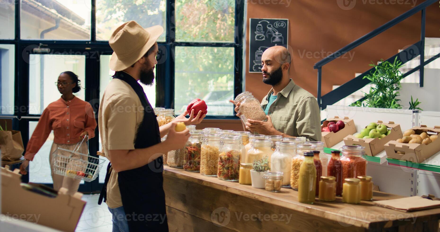 Vendor offers buyer bulk products, presenting middle eastern shopper selection of pasta, herbs and sauces. Young man buying organic produce at nearby eco friendly supermarket. Handheld shot. photo