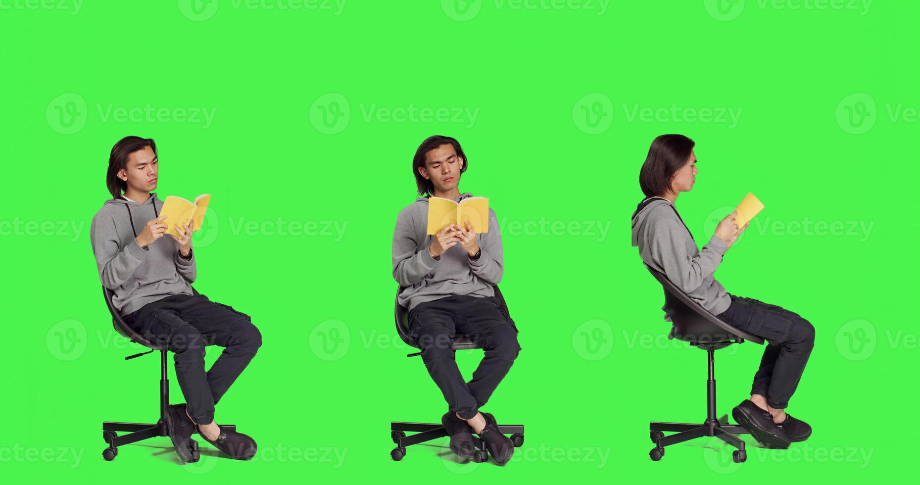 Asian guy reading literature book over greenscreen backdrop, enjoying lecture while he sits on chair in studio. Person reads fiction novel story, being interested in classic leisure activities. photo