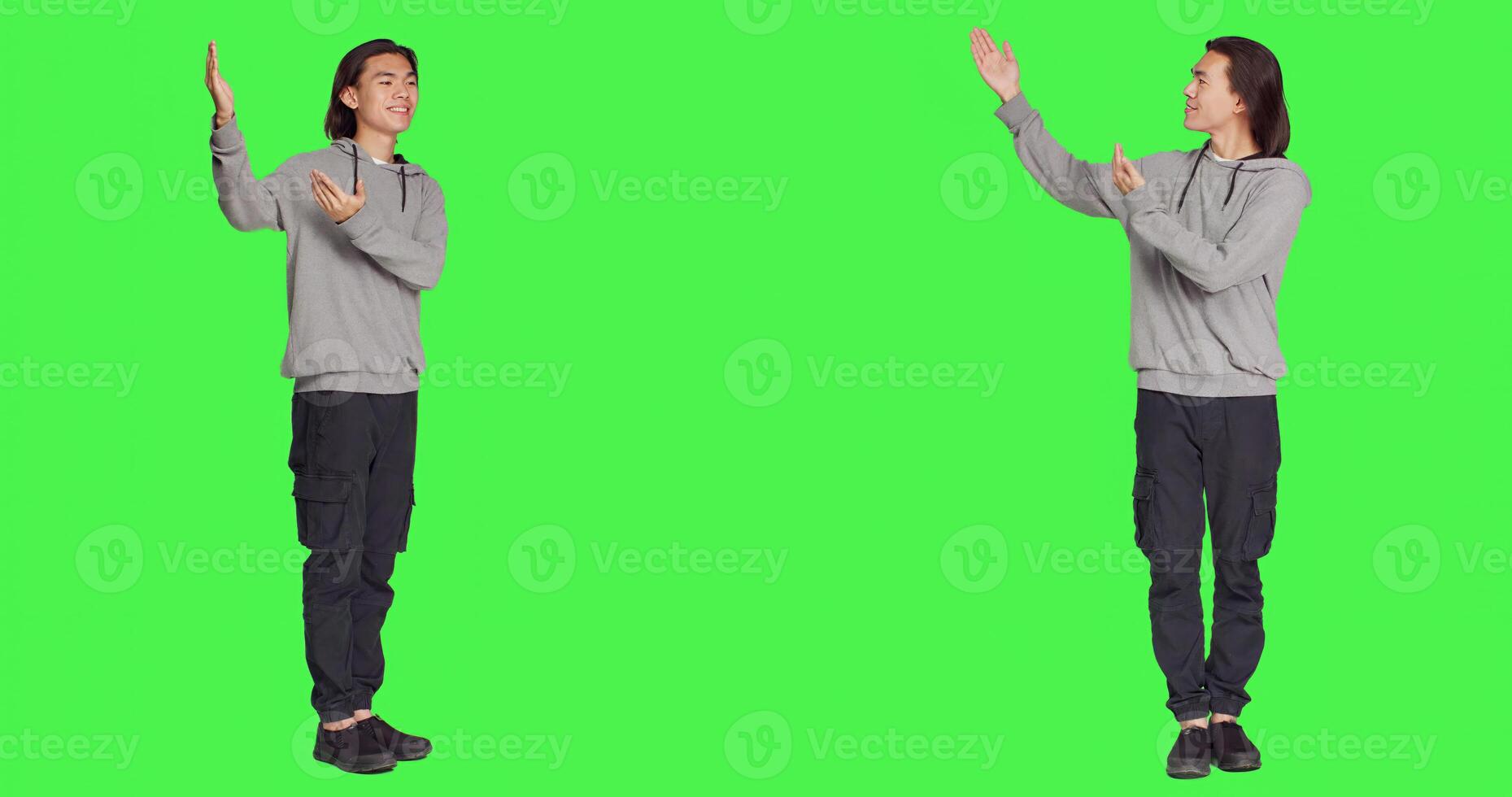 Asian person works on marketing ad in studio, pointing to left or right sides for new advertisement campaign. Young male model smiling and working on commercial, standing over greenscreen. photo
