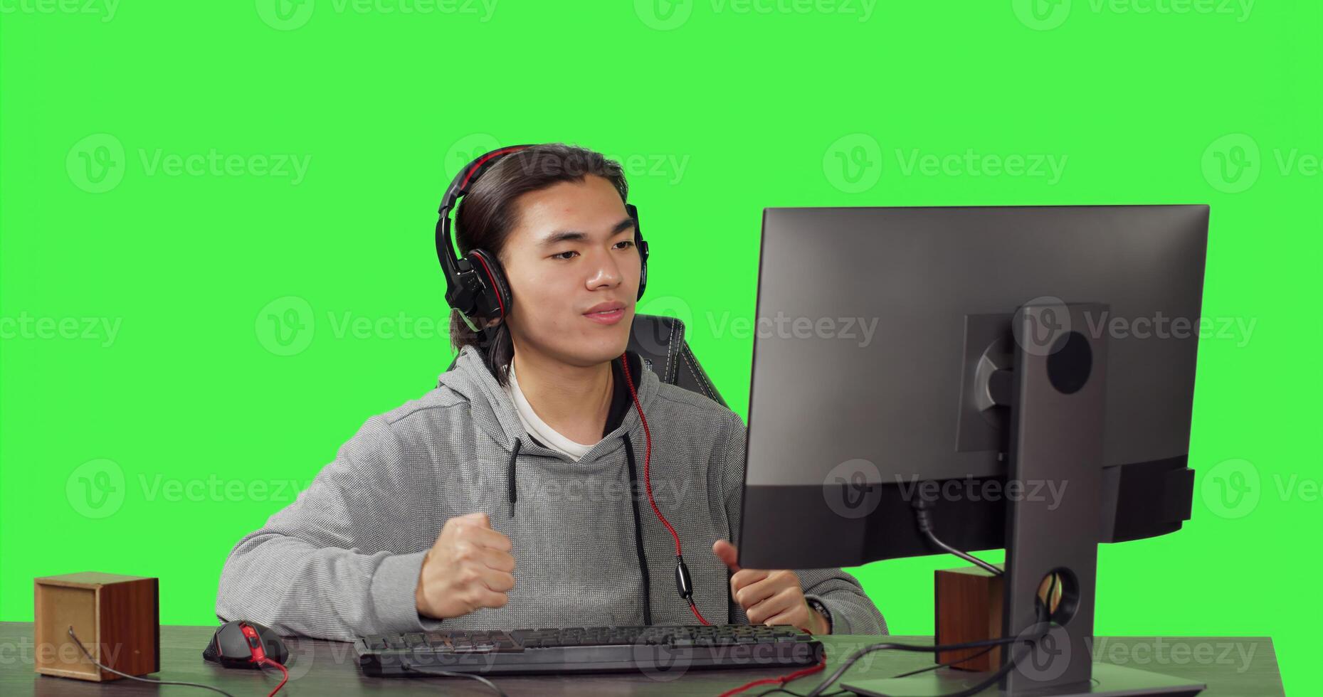 Asian player gaming on computer at desk, playing online videogames with people. Young adult having fun with rpg competition, speaking to friends on headphones over greenscreen. photo